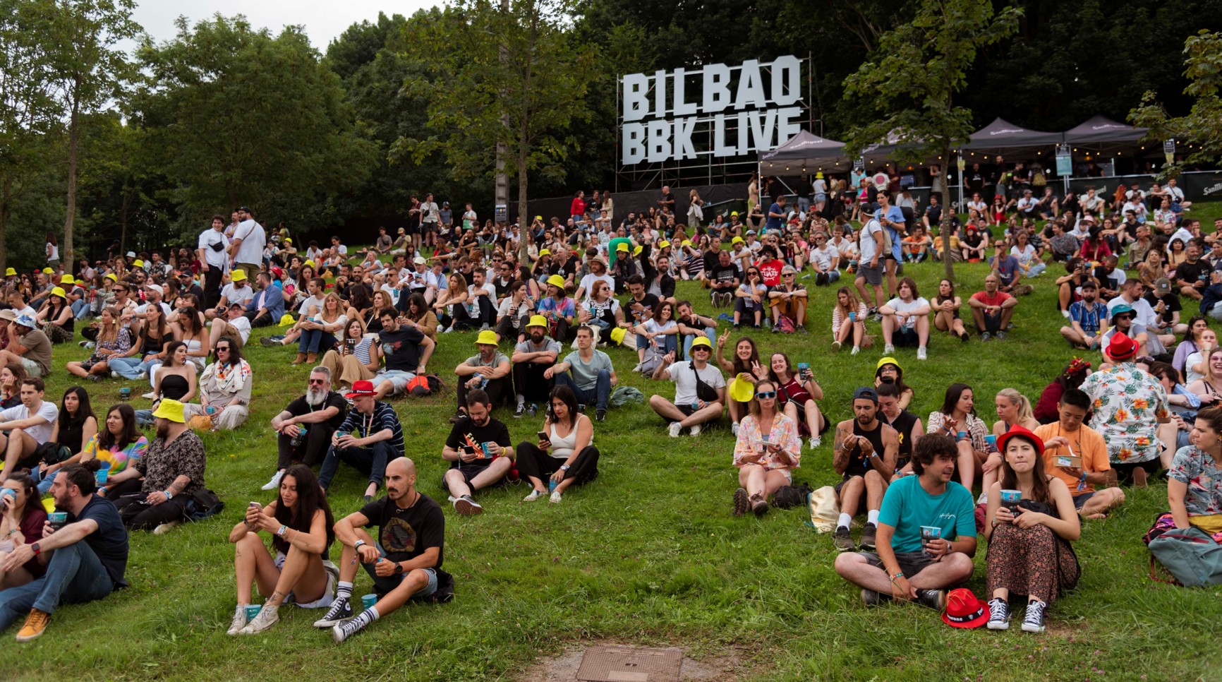Grupo de personas en una colina durante el festival Bilbao BBK LIVE, con un bosque al fondo.