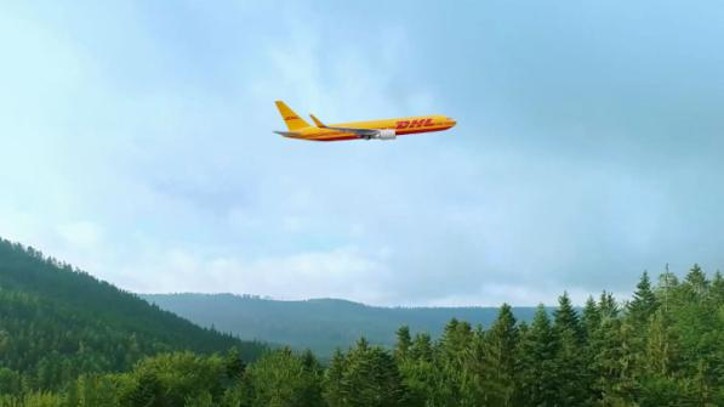Avión DHL sobrevolando montañas y bosques verdes bajo cielo nublado.