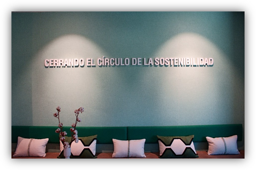 Pared verde con la frase ‘Cerrando el círculo de la sostenibilidad’ y un banco con varios cojines decorativos.