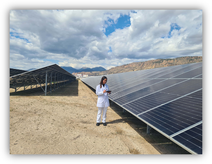 Persona con bata blanca revisando una tableta junto a grandes paneles solares en un campo al aire libre