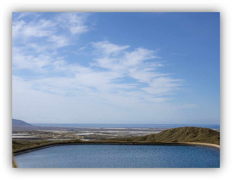 Depósito de agua en una zona elevada con vista a la costa y al mar bajo un cielo despejado.