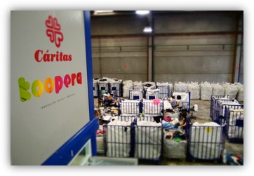 Interior de una nave de Cáritas Koopera con personas clasificando ropa en grandes contenedores.