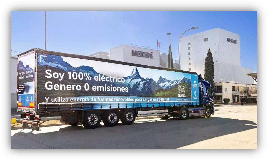 Camión eléctrico con mensaje sobre cero emisiones estacionado frente a una fábrica industrial.