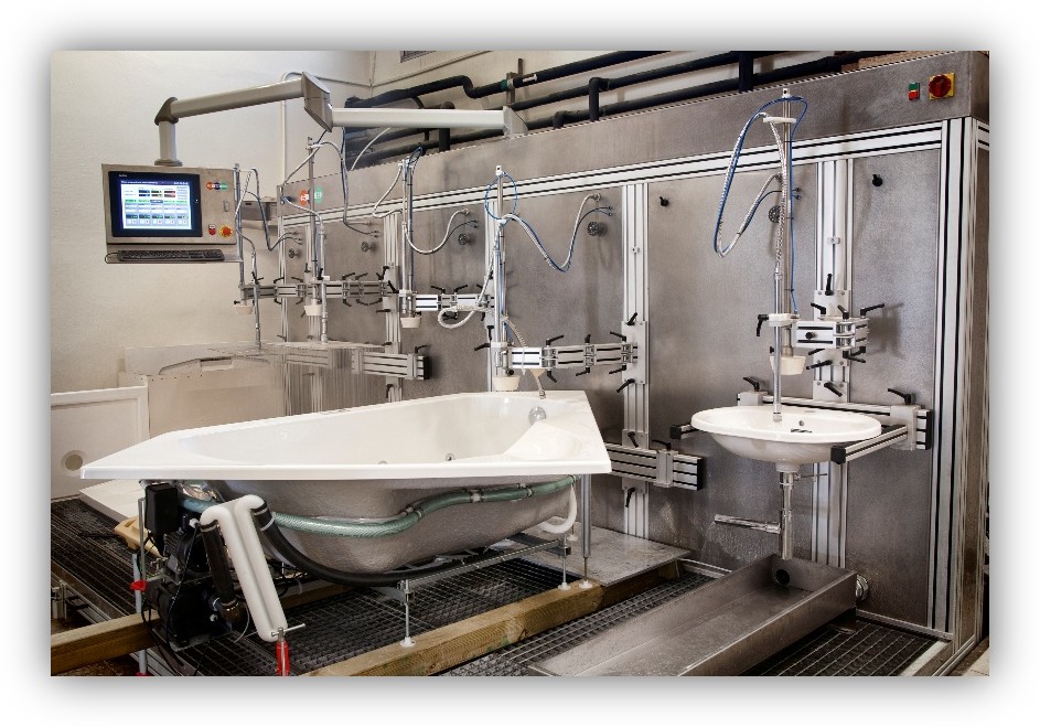 Instalación industrial de pruebas con una bañera y un lavabo conectados a equipos y tuberías.