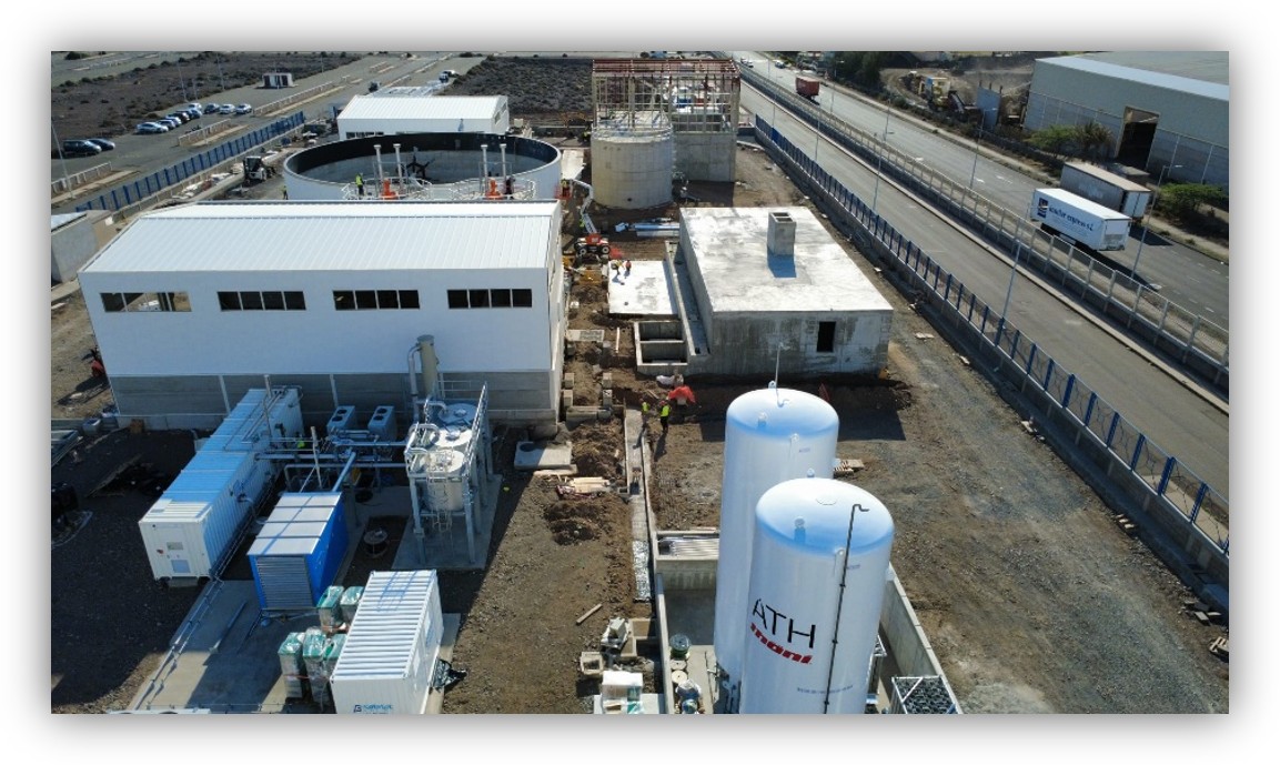 Vista aérea de una instalación industrial con tanques, edificios y equipos técnicos, situada junto a una carretera.
