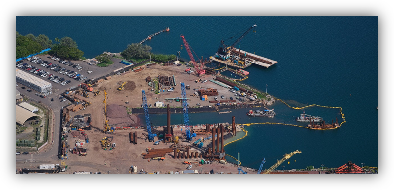 Vista aérea de un puerto en obras con grúas, maquinaria y estructuras de construcción sobre el agua.