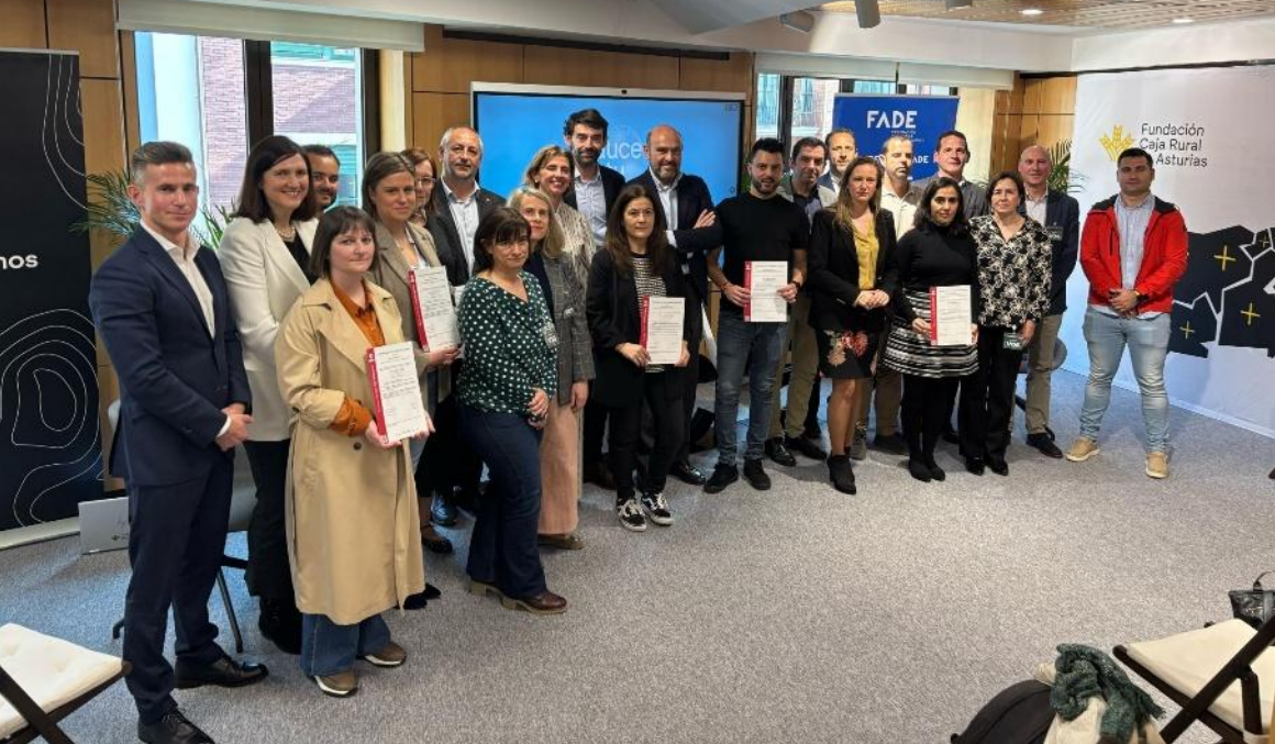 Grupo de personas posando en una sala durante un acto de reconocimiento. Varias sostienen certificados. Al fondo aparecen paneles con los logotipos de FADE y Fundación Caja Rural de Asturias.