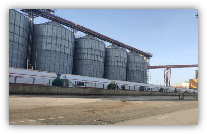 Grandes silos industriales metálicos alineados con una cinta transportadora en una planta exterior.
