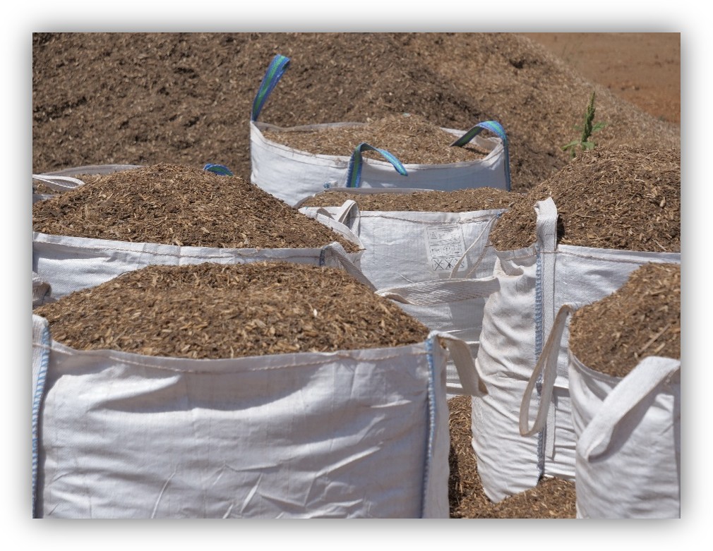 Sacos grandes llenos de material orgánico triturado, como restos vegetales o compost, almacenados en un terreno