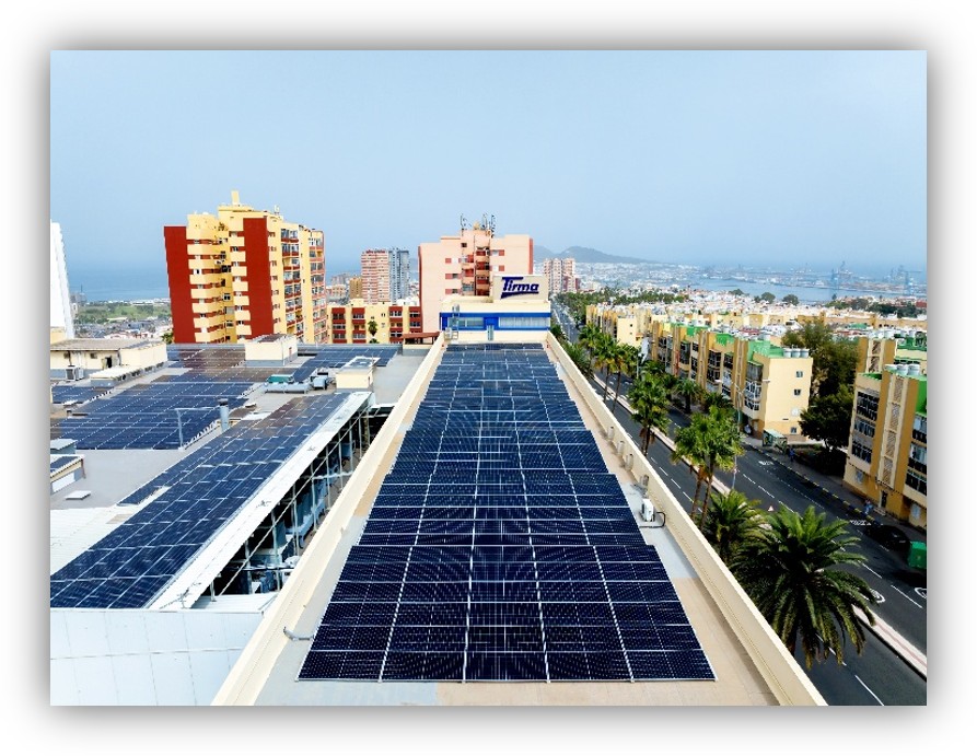 Cubierta de un edificio urbano con paneles solares fotovoltaicos instalados, rodeada de edificios residenciales y con el mar al fondo.