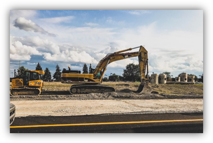 Excavadora trabajando en una obra de movimiento de tierras junto a una carretera, en un terreno abierto.