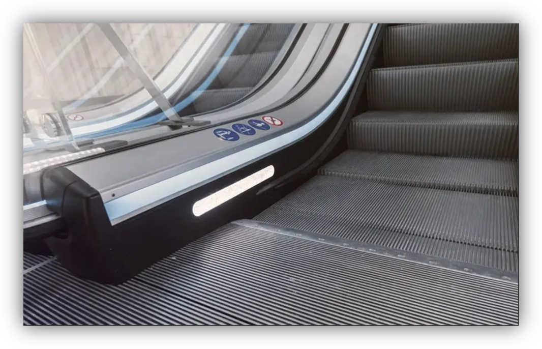 Primer plano de una escalera mecánica con iluminación lateral y señalización de seguridad en el pasamanos.