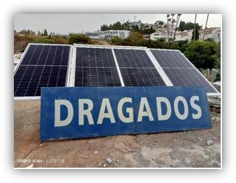 Panel informativo con el nombre Dragados situado frente a una instalación de paneles solares fotovoltaicos sobre una cubierta.