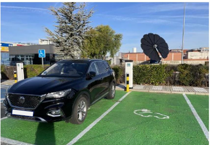 Vehículo en una plaza verde con cargadores eléctricos y panel solar en forma de flor al fondo.