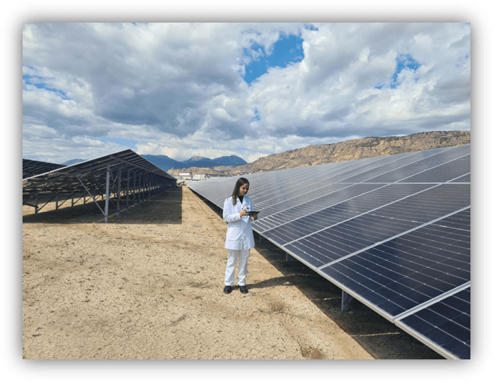 Persona con bata blanca revisando una tableta junto a grandes paneles solares en un campo al aire libre