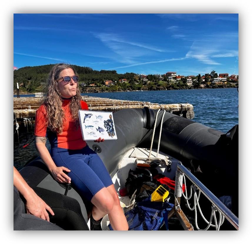 Persona sentada en una embarcación inflable mostrando una lámina con ilustraciones de animales marinos, con el mar y edificaciones al fondo.