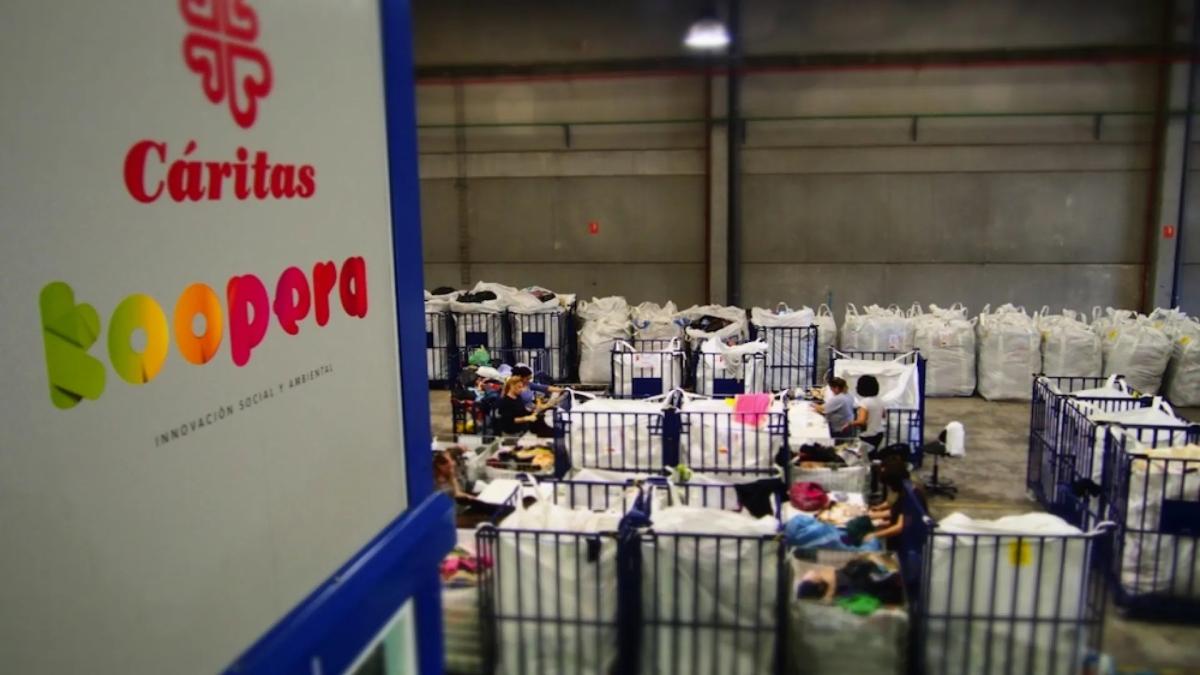 Interior de una nave de Cáritas Koopera con personas clasificando ropa en grandes contenedores.