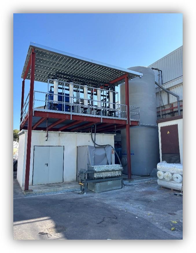 Instalación industrial con sistema de filtración por membranas elevado, depósitos cilíndricos y equipos técnicos en una planta exterior.