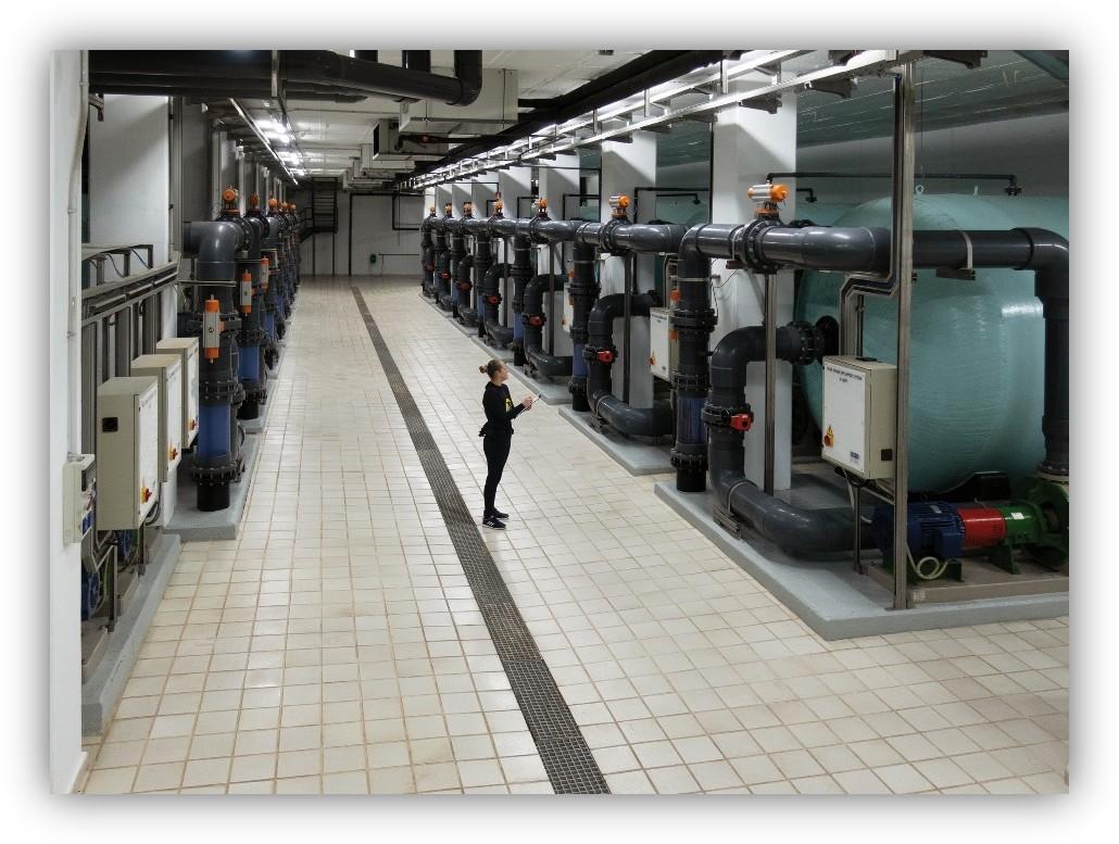 Técnica revisando una instalación industrial de tratamiento de agua con tuberías y equipos.