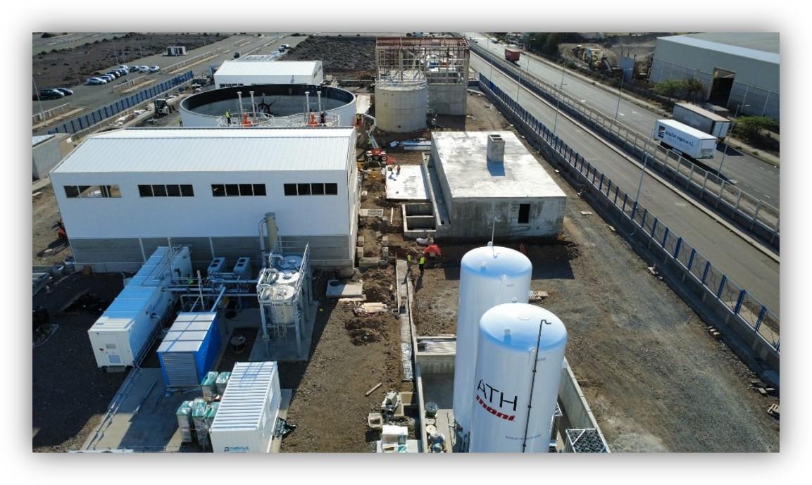 Vista aérea de una instalación industrial con tanques, edificios y equipos técnicos, situada junto a una carretera.