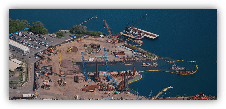 Vista aérea de un puerto en obras con grúas, maquinaria y estructuras de construcción sobre el agua.