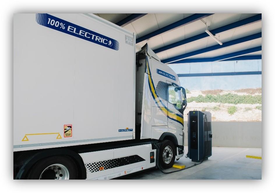 Camión eléctrico de mercancías conectado a un punto de recarga en una nave industrial.