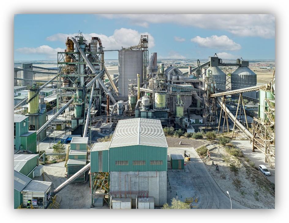 Planta industrial con estructuras metálicas, tuberías, silos y cintas transportadoras en un entorno abierto.