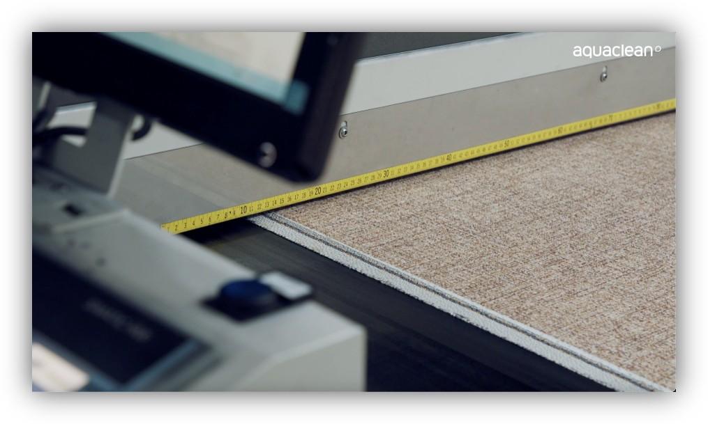 Detalle de una máquina industrial midiendo y cortando material textil o revestimiento con una cinta métrica visible.