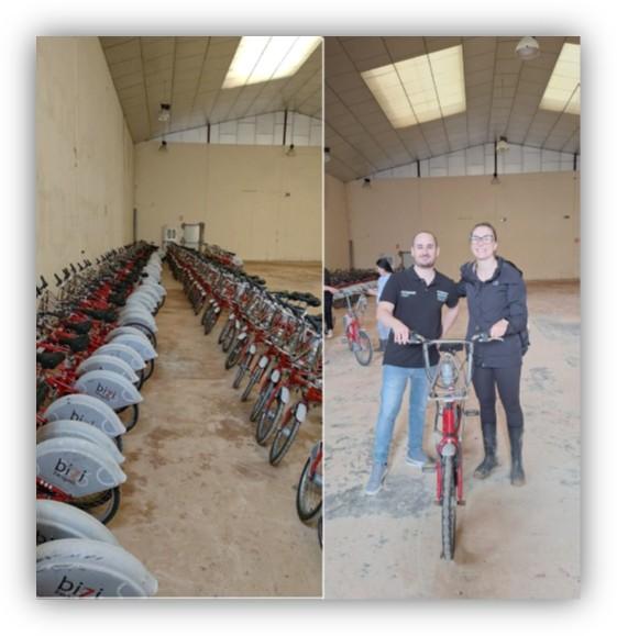 Interior de una nave con filas de bicicletas aparcadas y, a la derecha, dos personas posando junto a una bicicleta.