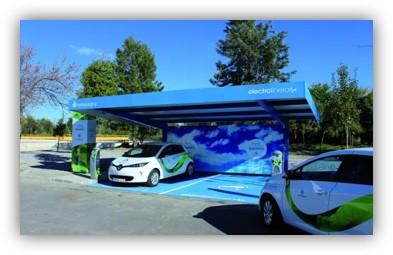 Punto de recarga para coches eléctricos con marquesina solar y vehículos estacionados bajo una estructura al aire libre.