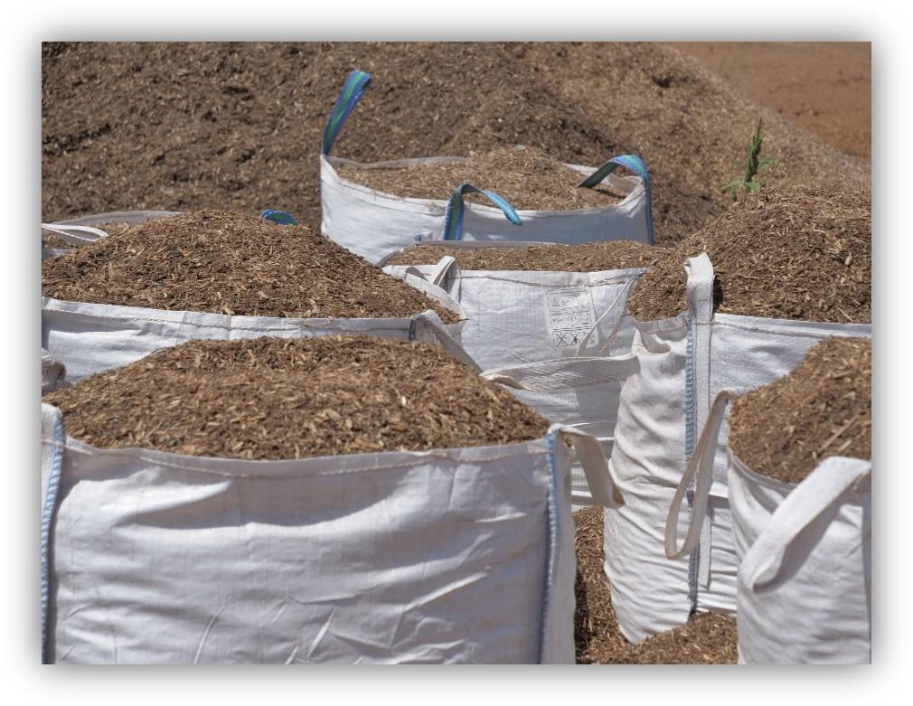 Sacos grandes llenos de material orgánico triturado, como restos vegetales o compost, almacenados en un terreno