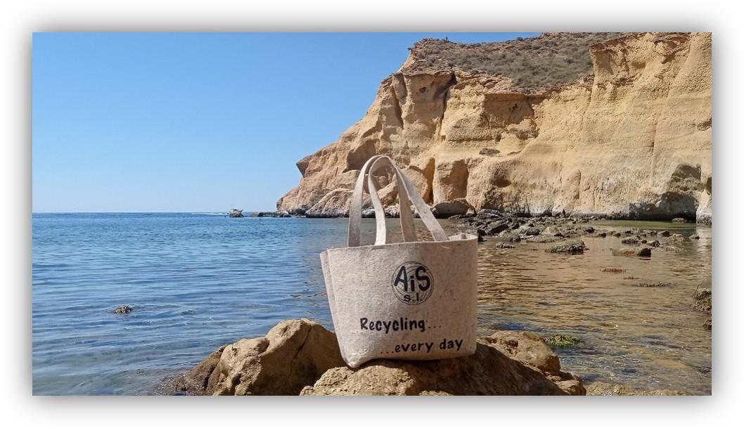 Bolsa reutilizable con el mensaje ‘Recycling every day’ colocada sobre unas rocas junto al mar, con acantilados al fondo.