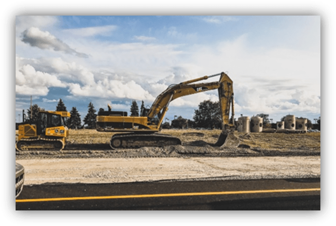 Excavadora trabajando en una obra de movimiento de tierras junto a una carretera, en un terreno abierto.