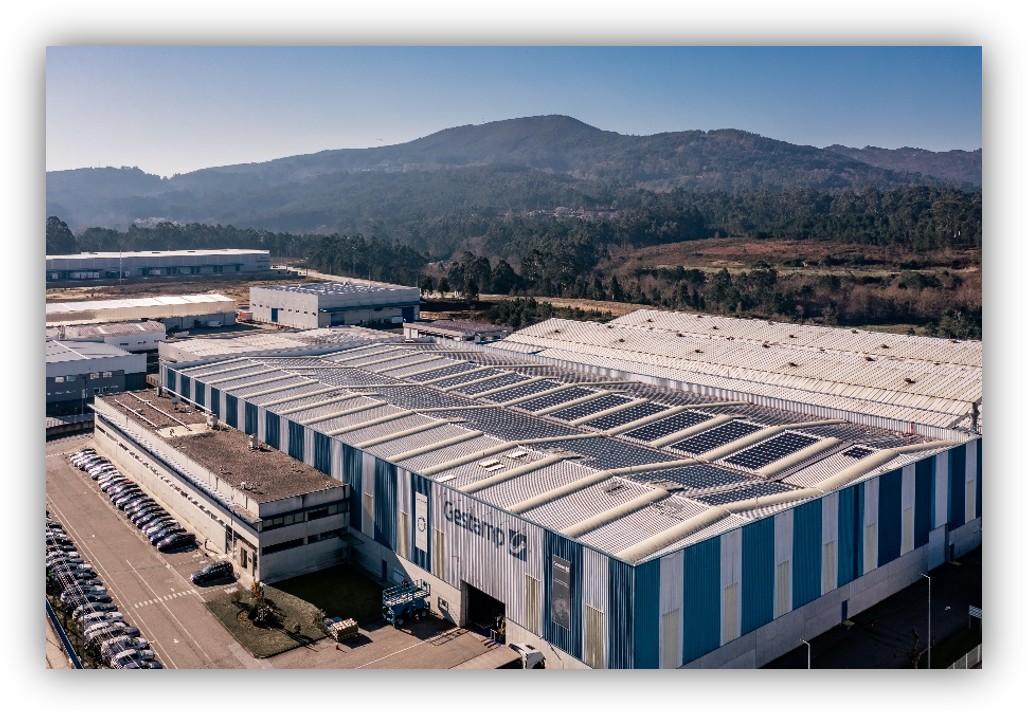Vista aérea de una planta industrial de Gestamp con paneles solares instalados en la cubierta, rodeada de zonas industriales y montañas
