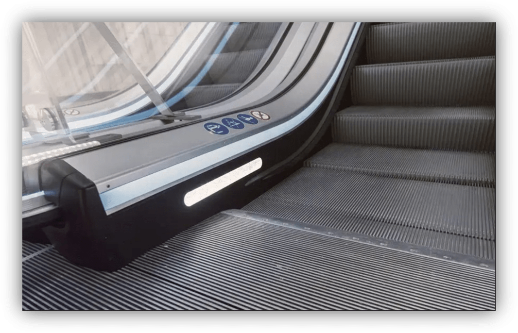 Primer plano de una escalera mecánica con iluminación lateral y señalización de seguridad en el pasamanos.