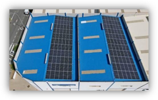 Vista aérea de una nave industrial con cubierta azul equipada con amplias filas de paneles solares fotovoltaicos.