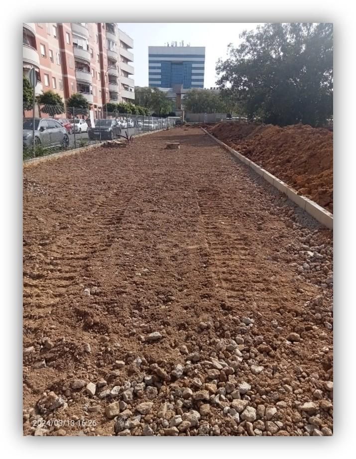 Zona en obras para la creación o mejora de un espacio urbano, con terreno nivelado, bordillos instalados y edificios residenciales al fondo.