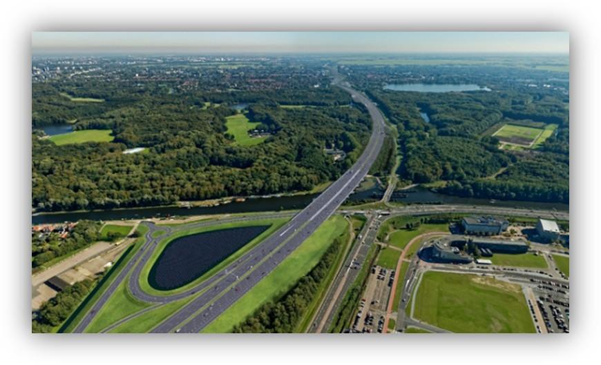 Vista aérea de una autopista rodeada de amplias zonas verdes, masas forestales y cursos de agua, mostrando una infraestructura integrada en el entorno natural.
