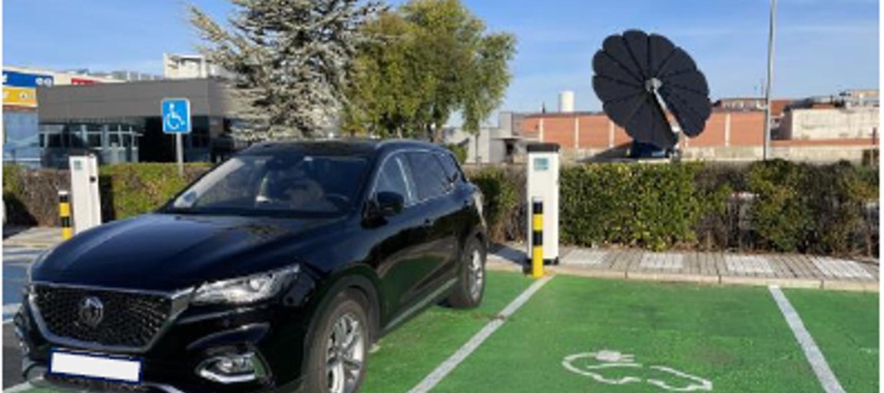 Vehículo en una plaza verde con cargadores eléctricos y panel solar en forma de flor al fondo.