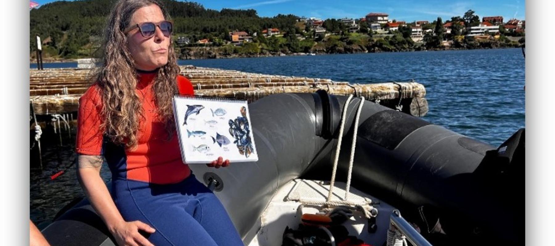 Persona sentada en una embarcación inflable mostrando una lámina con ilustraciones de animales marinos, con el mar y edificaciones al fondo.