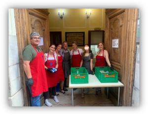 Grupo de personas con delantales junto a una mesa con cajas verdes en la entrada de un edificio