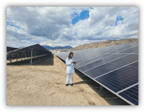 Persona con bata blanca revisando una tableta junto a grandes paneles solares en un campo al aire libre