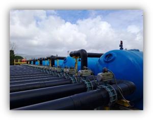 Instalación industrial con grandes tuberías negras y depósitos azules alineados al aire libre bajo un cielo nublado.