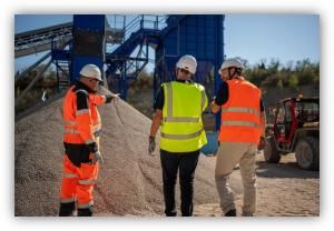 Personas con cascos y chalecos de seguridad supervisan material a granel en una instalación industrial.
