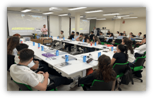 Personas participan en una sesión formativa sobre sostenibilidad en un aula con mesas y una presentación proyectada