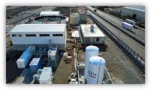 Vista aérea de una instalación industrial con tanques, edificios y equipos técnicos, situada junto a una carretera.