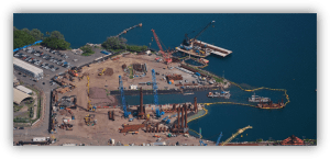 Vista aérea de un puerto en obras con grúas, maquinaria y estructuras de construcción sobre el agua.