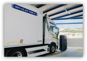 Camión eléctrico de mercancías conectado a un punto de recarga en una nave industrial.