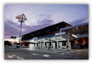 Estación de recarga de vehículos eléctricos frente a un complejo comercial al atardecer.