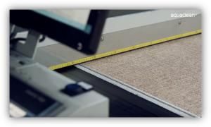 Detalle de una máquina industrial midiendo y cortando material textil o revestimiento con una cinta métrica visible.